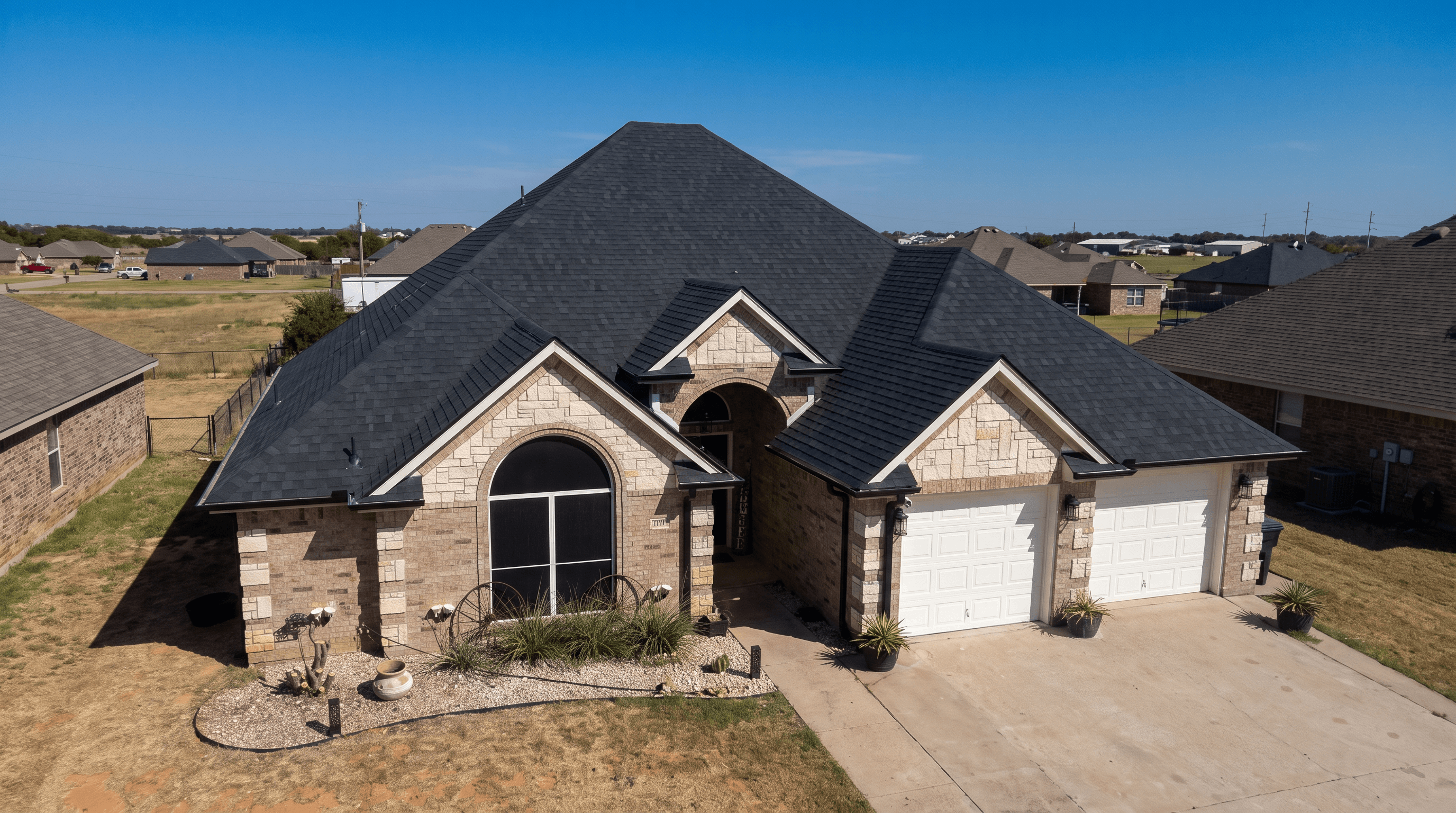 Suburban home with tan brick, stone accents, and a prominent multi-gabled black shingle roof.